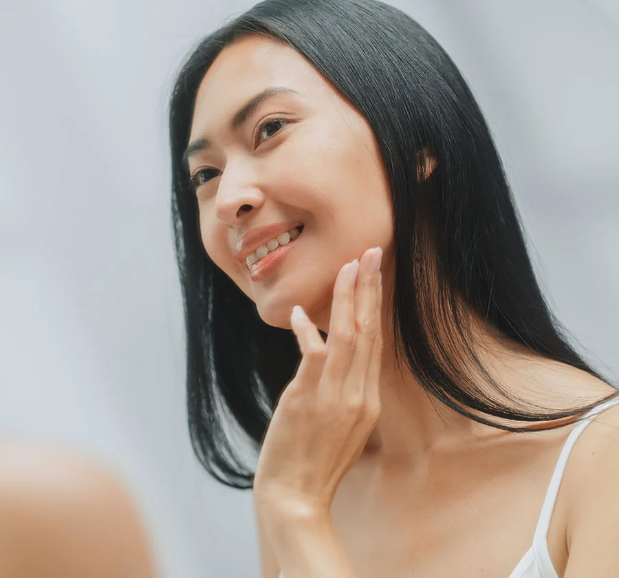 Close-up of a woman gently touching her face, showcasing a moment of self-care and appreciation for her natural beauty. Her soft smile and gentle touch convey a sense of contentment and self-love. The soft lighting and blurred background draw attention to her radiant features. - PRF in Thiensville, WI