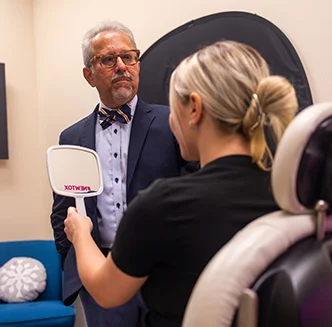 Dr. Siddiqui looking at his patient as she looks at her reflection in a hand held mirror - Regenerative Medicine in Thiensville, WI